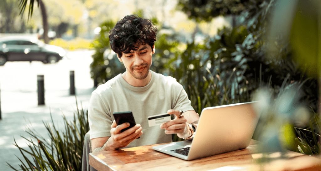 Man staring at his phone and credit card in front of a laptop