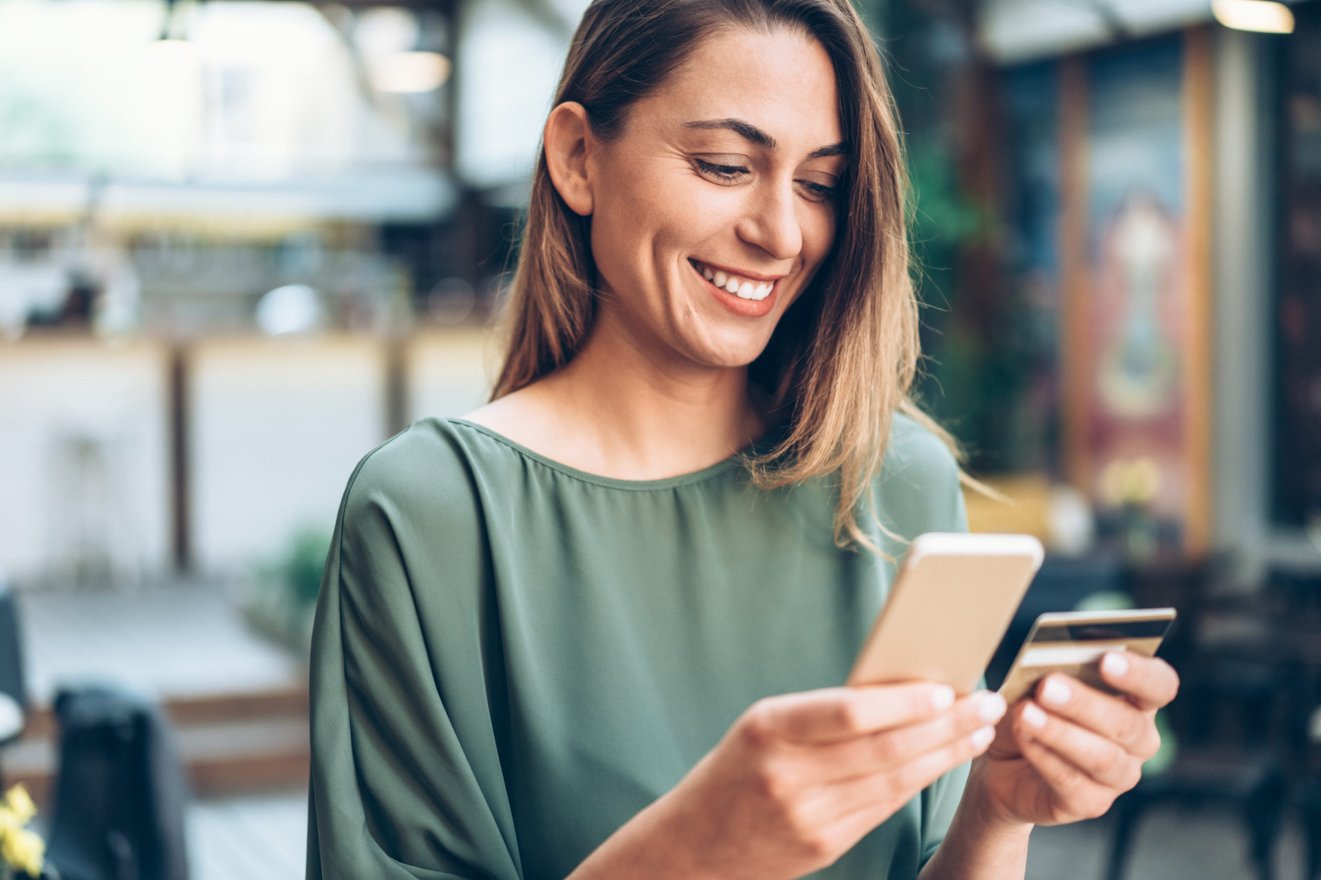 Young woman shopping online in cafe using smartphone and credit card