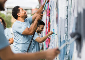 The group of coworkers smile while they help paint the graffiti wall.