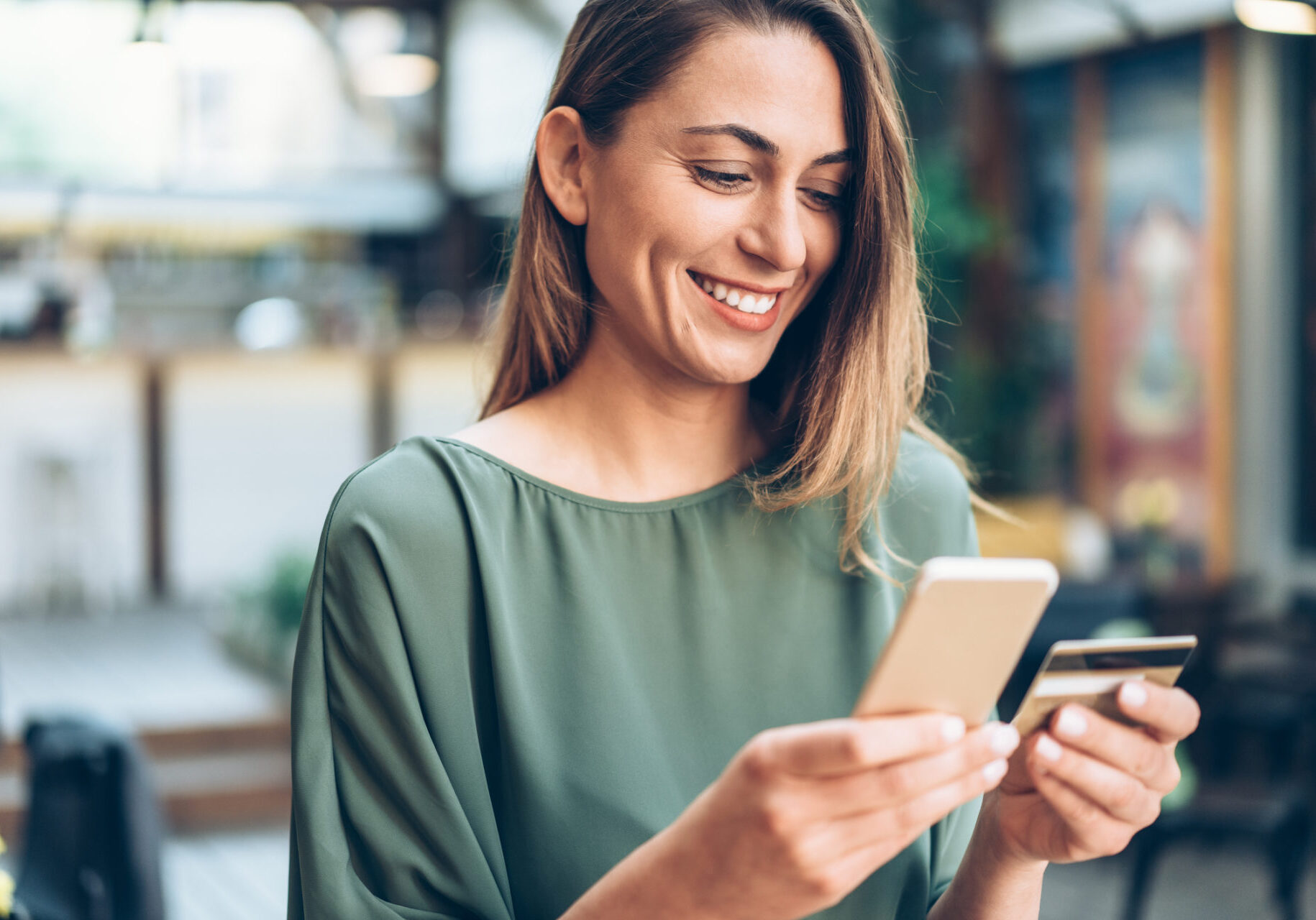 Young woman shopping online in cafe using smartphone and credit card